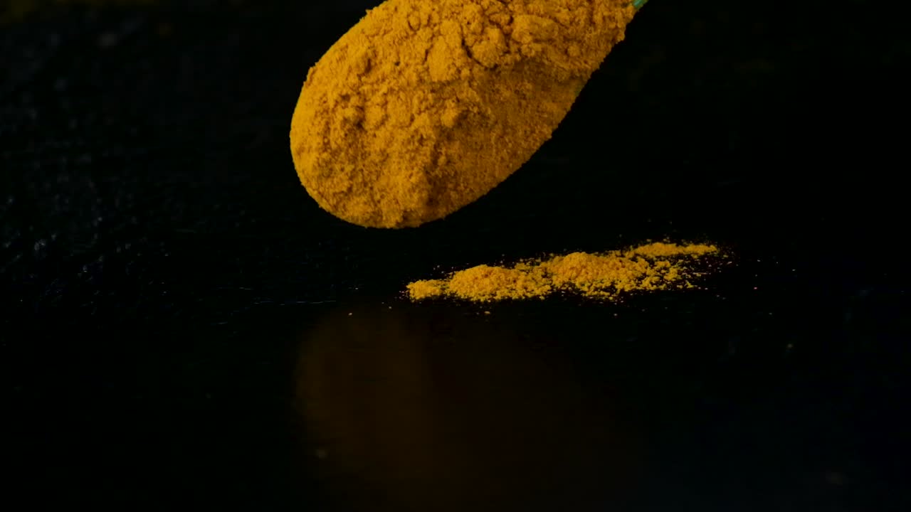 Turmeric powder dropping on a black table surface from a spoon with black background