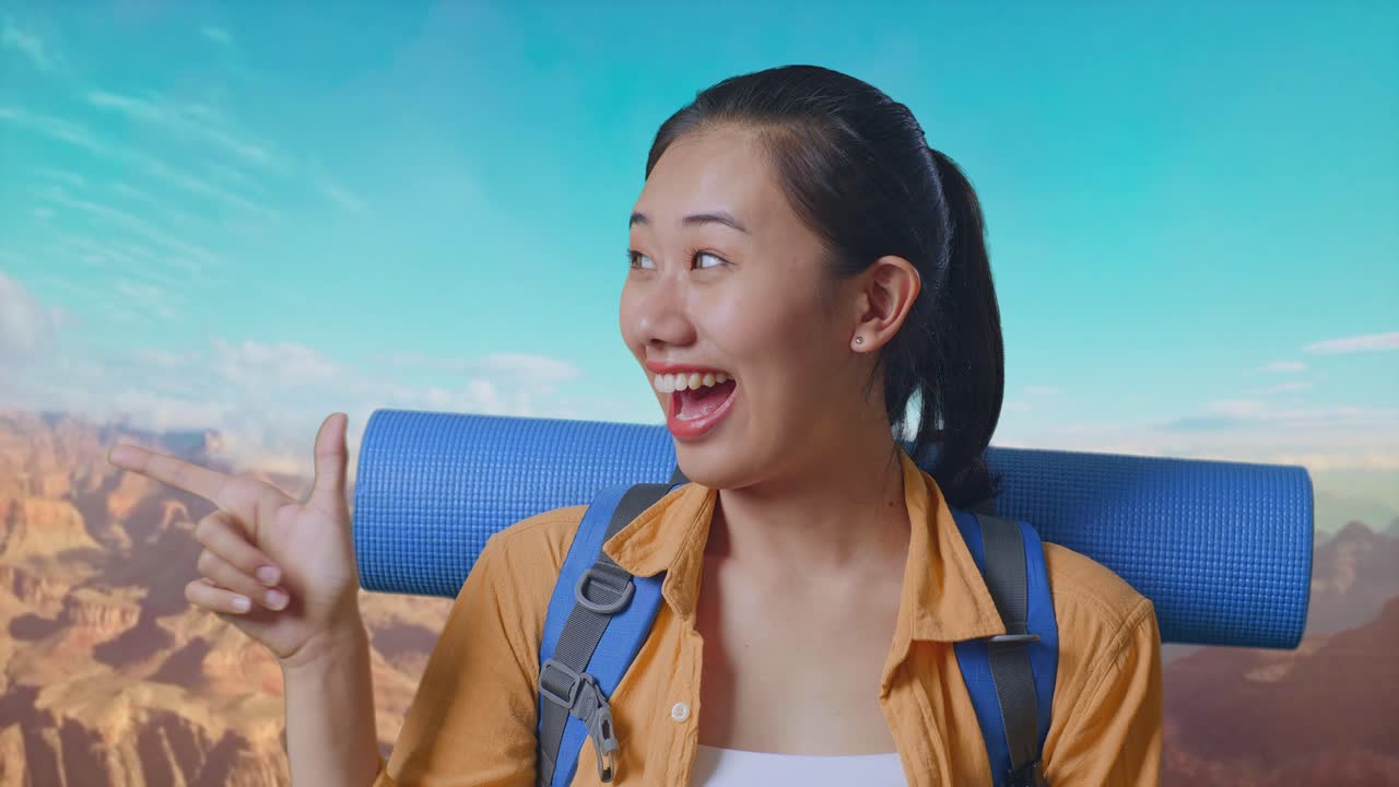 Close Up Of Asian Female Hiker With Mountaineering Backpack Smiling And Pointing To Side While Traveling At The Top Of Mountain
