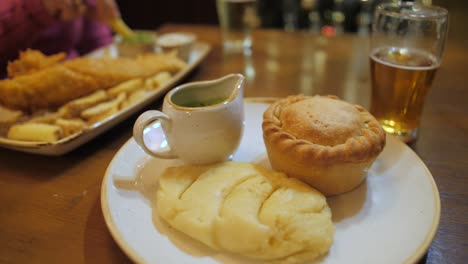 pie and mash served with liquor with a plate of fish and chips in the background