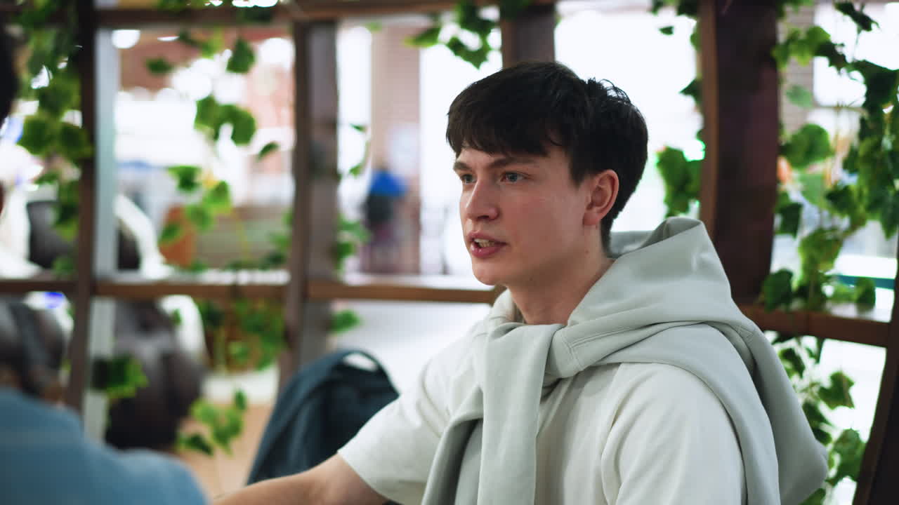 young student wearing white polo listening seriously to friend during intense discussion, focused expression, with blurred background, subtle body language showing engagement and thoughtfulness