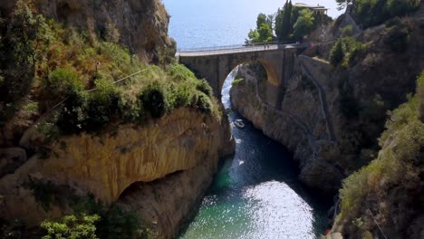 fiordo di furore arch bridge with a boat entering the passageway to village, amalfi coast in salerno italy, aerial approach down shot