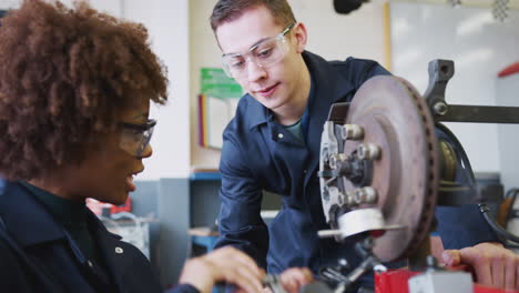 tutor with female students checking car brake discs on auto mechanic course at college