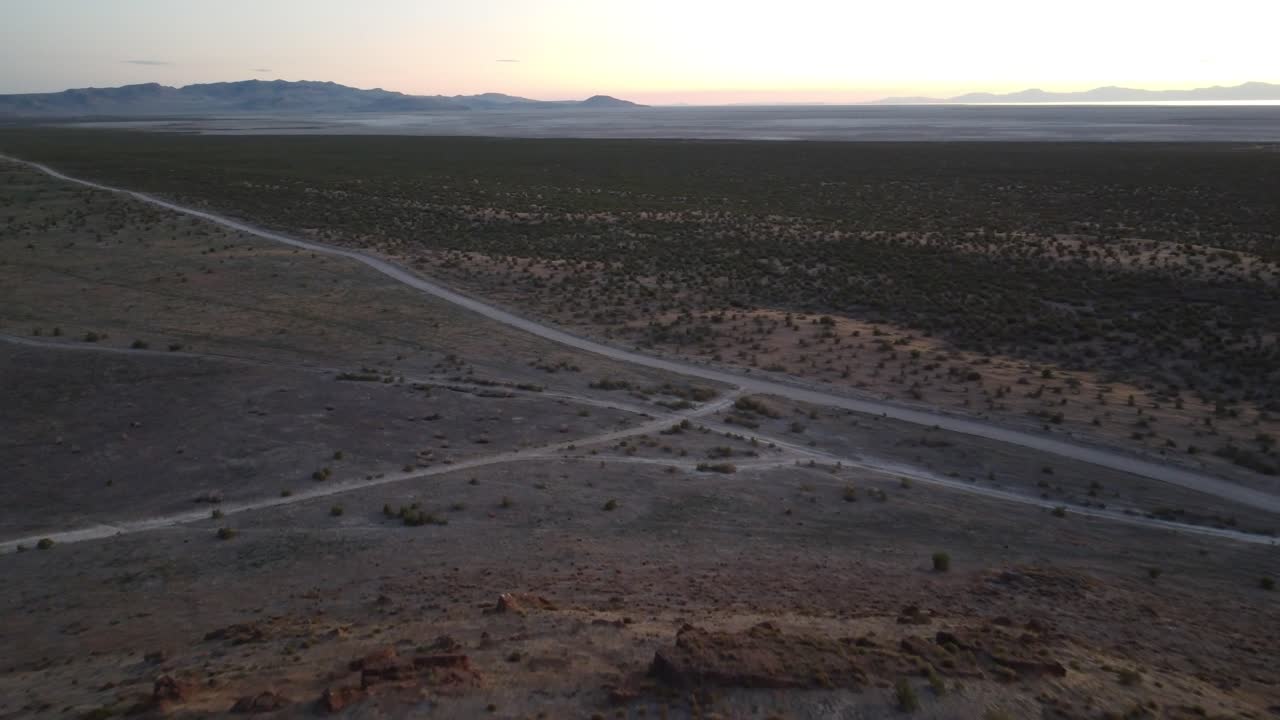 Drone clip of a long dirt road through barren Utah desert land with subtle sunset colors and distant rock formations creating a scenic and atmospheric view