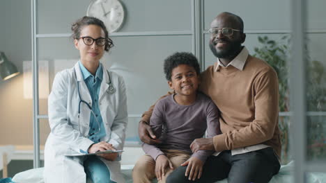 portrait of positive female doctor, african american boy and his dad in clinic