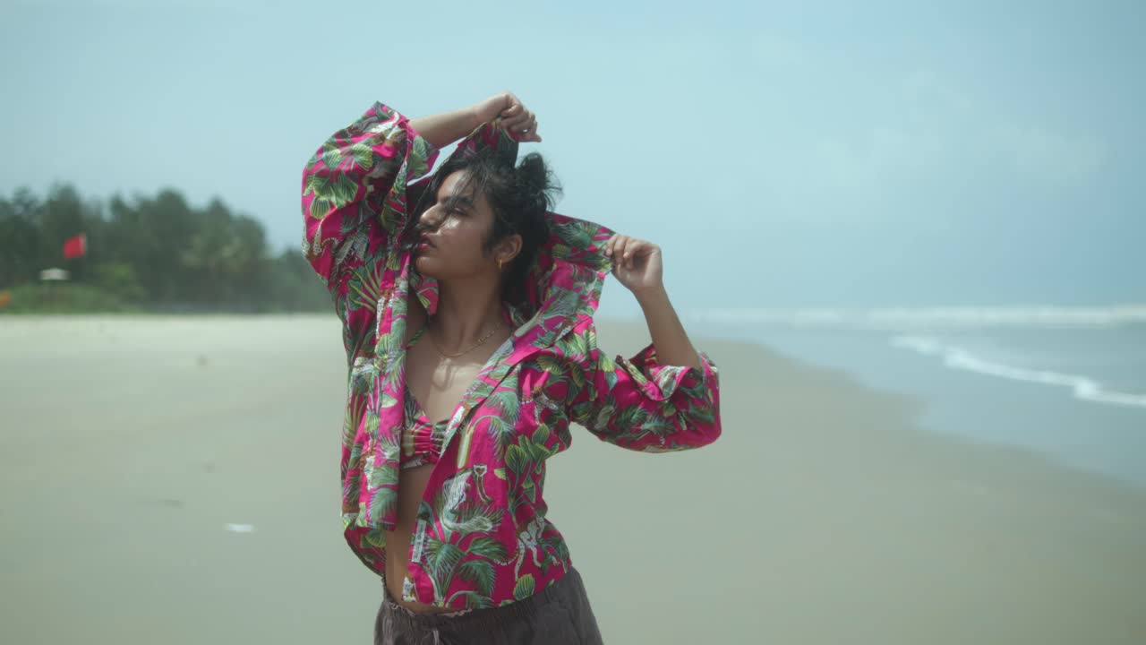 Confident woman raising face and arms to the sky in vibrant outfit on beach