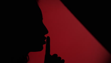 side view of faded female face placing her finger on lips on dark red background