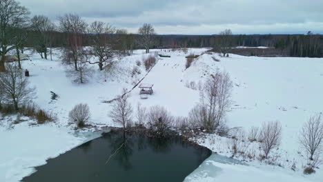 aerial drone shot over a pond partially frozen surrounded by snow covered landscape on a cold winter day