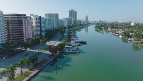 Modern-tall-town-development,-multilane-road-lined-by-palm-trees-and-turquoise-water-in-creek.-Miami,-USA