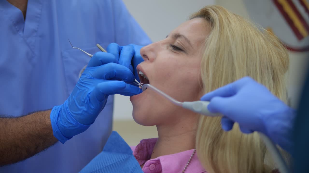 Ortodontista masculino utiliza instrumentos odontológicos para examinar os dentes de uma mulher loira. Cuidados odontológicos