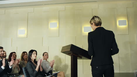 joven empresaria caucásica entrando en una sala de conferencias mientras la gente aplaudía, luego sube al podio