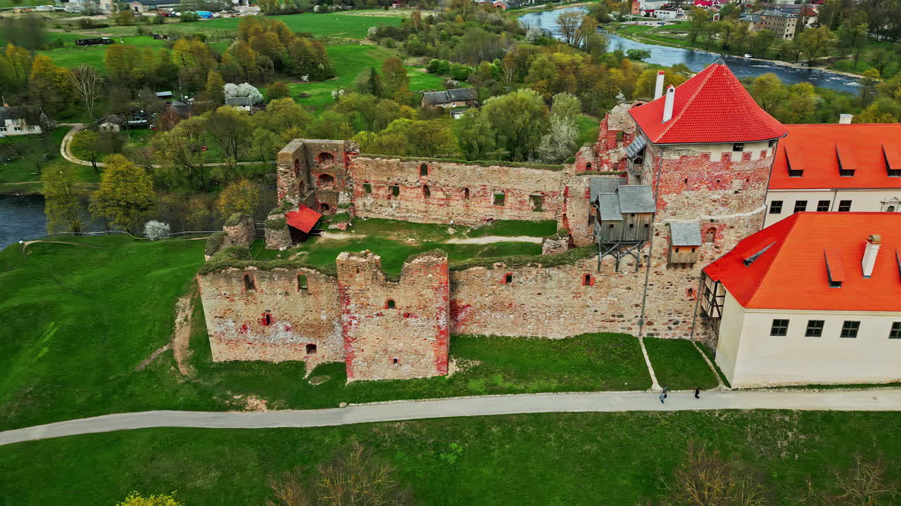 라트비아의 휘어지는 강을 따라 바우스카 성 박물관 위를 는 드론