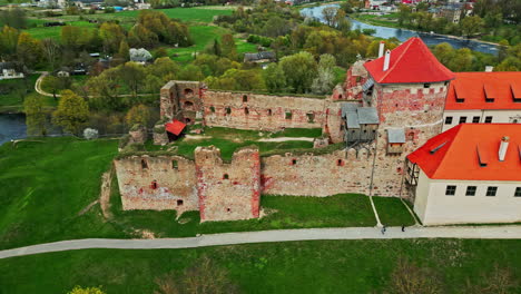 aerial drone panning shot over bauska castle museum alongside a winding river in latvia