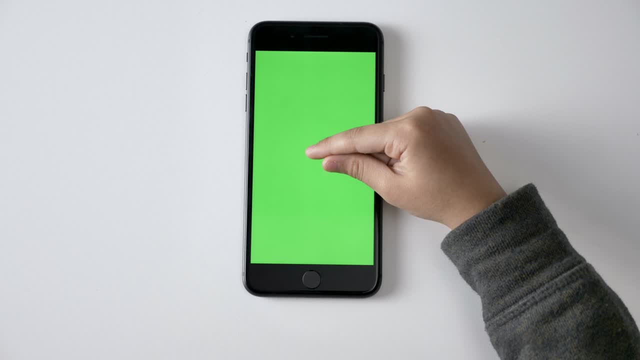Mani di bambini che fanno il gesto di "pinch to zoom" su uno smartphone, schermo verde, concetto di chromakey, ripresa dall'alto 60 fps.