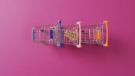 video of black friday text on cardboard on shopping trolleys on pink background