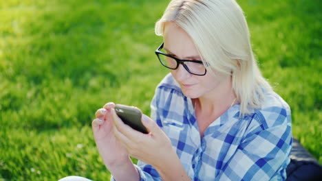 portrait of a young woman wearing glasses enjoying a smartphone in the park beautiful sun glare 4k s