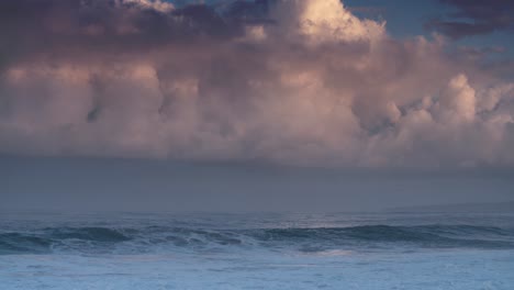 blue waves roll into the coast of hawaii in slow motion with pink clouds background