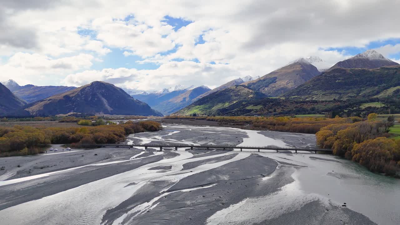 Aerial view of a winding river through lush valleys and mountains under a partly cloudy sky in Glenorchy