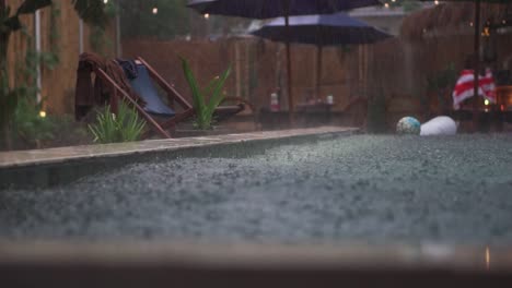 Low-angle-of-monsoon-rainstorm-falling-on-top-of-hotel-swimming-pool-causing-thousands-of-little-ripples-and-waves-in-asia