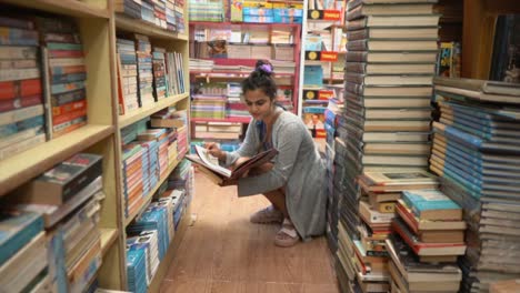 beautiful young asian girl sitting in the middle of bookshelves and reading, side angle tracking in shot