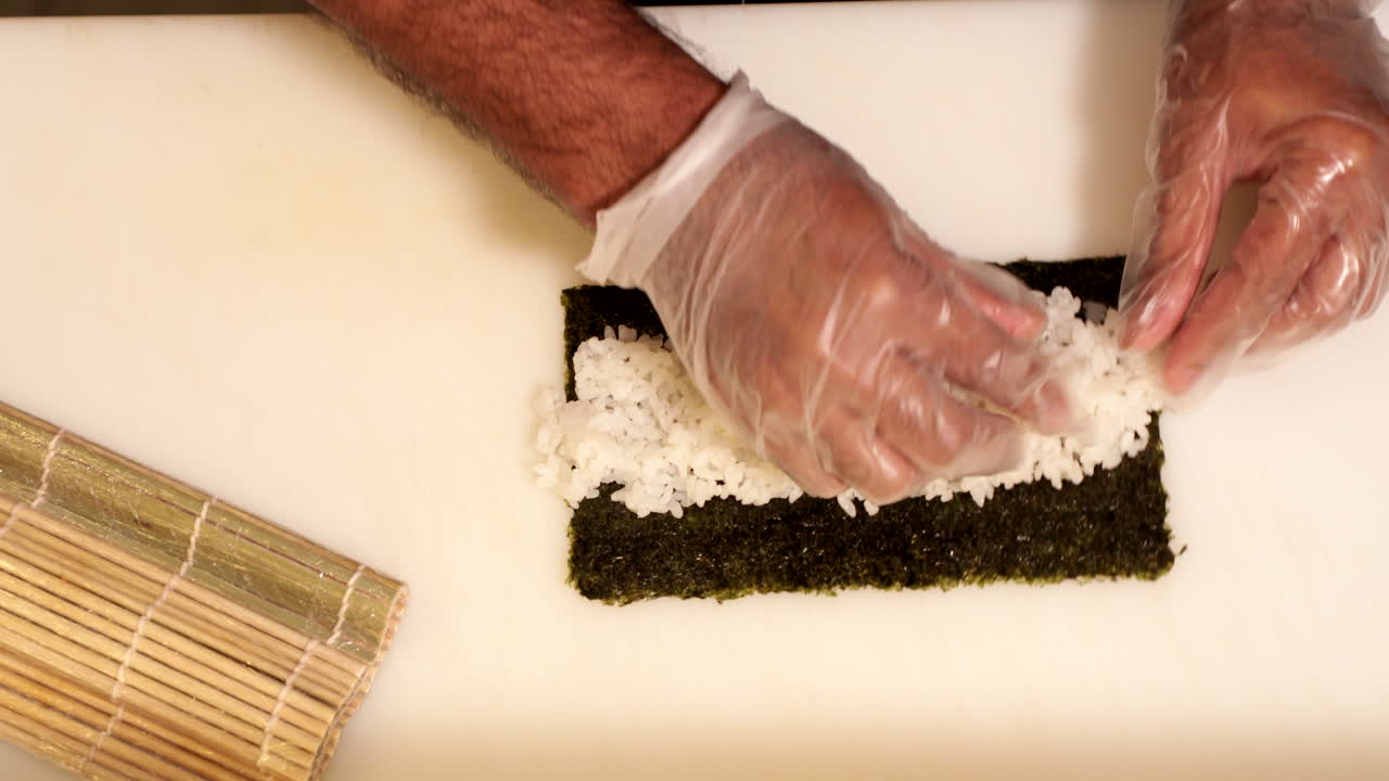 chef esparciendo arroz de sushi cocido en una envoltura de algas - toma cenital, cámara lenta
