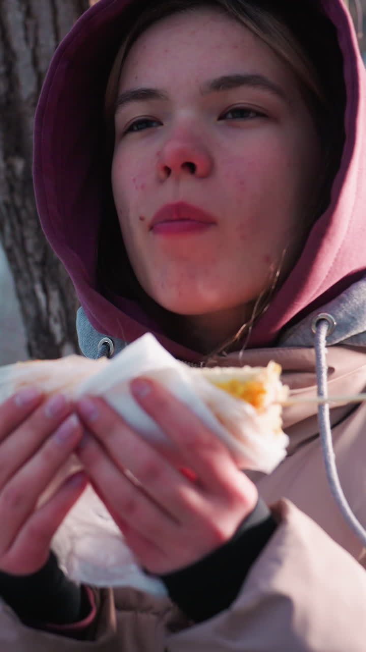 joven adulto con traje de invierno descansando en un árbol comiendo maíz bocadillo en un parque al aire libre durante el invierno, reflejo de luz desde el fondo añadiendo calor a la escena, parque de invierno momento de ocio
