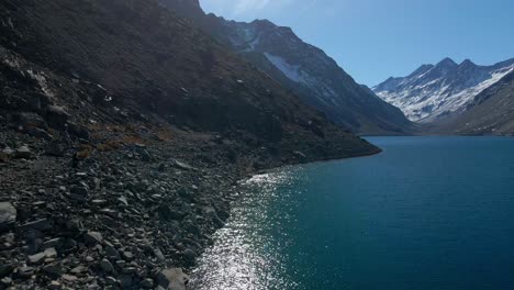 Dolly-in-aerial-view-of-the-shore-of-Laguna-del-Inca-with-snowcapped-mountains-in-the-background,-Los-Andes,-Chile