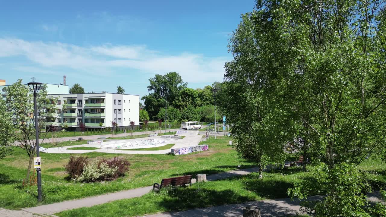 Sunny day at an urban skatepark next to apartment buildings with a bus passing by.