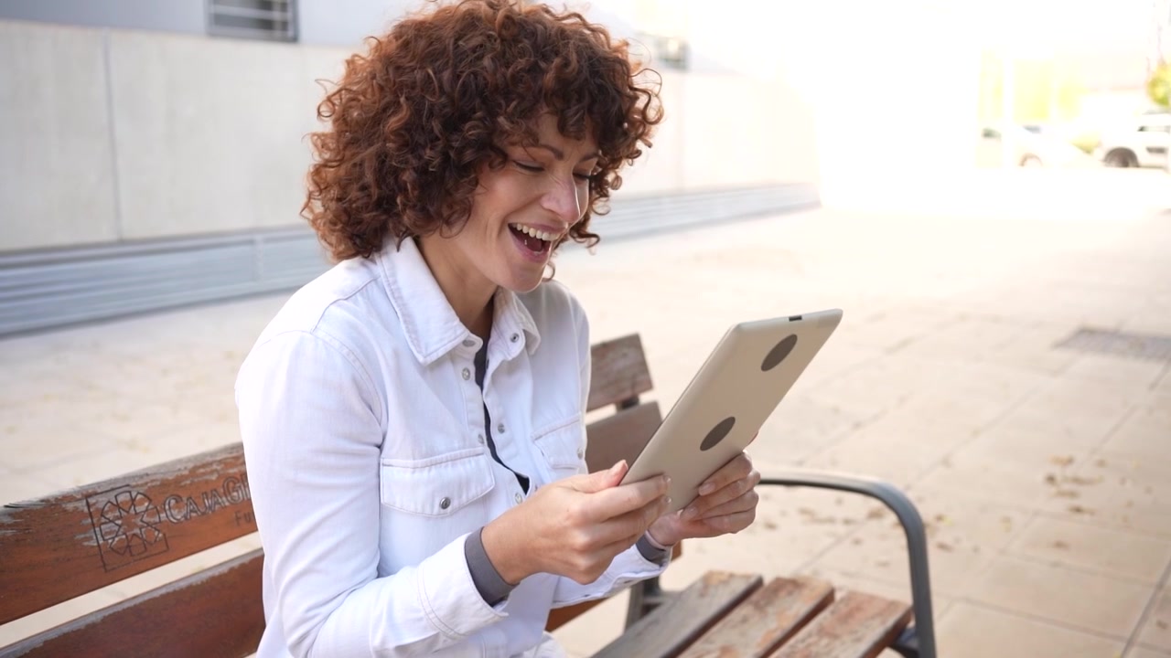 A young woman engaged with her tablet while sitting comfortably outdoors in an urban environment