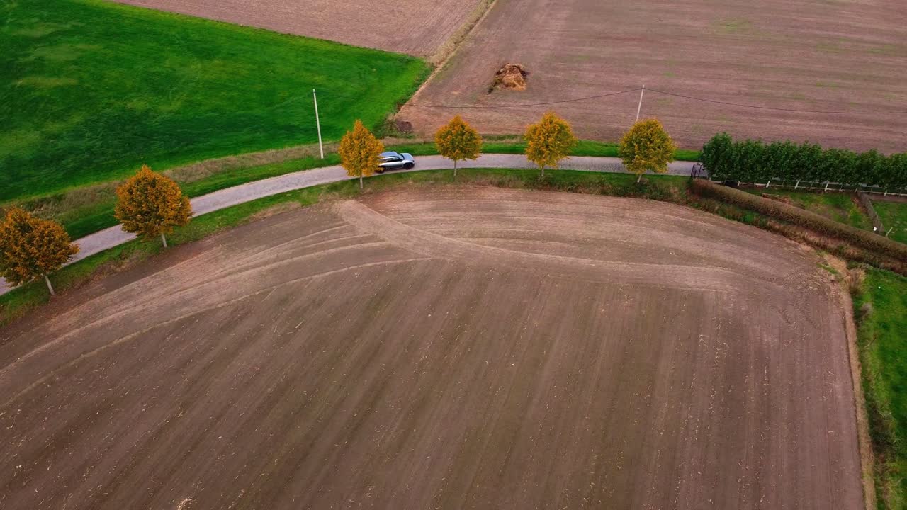 Car driving up a U-turn in between agricultural fields in the belgian countryside during autumn