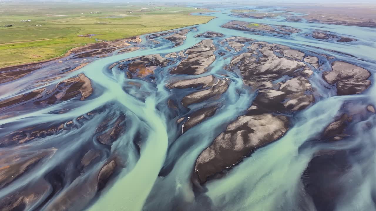 Flowing, braided glacial river water in Iceland flows through a flat green prairie area near Iceland's coast in summer