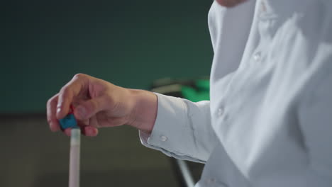 vista lateral de primer plano de un joven con camisa blanca, profundamente enfocado mientras aplica tiza al palo de señal. la expresión concentrada, la iluminación tenue y el fondo oscuro crean una atmósfera dramática de billar