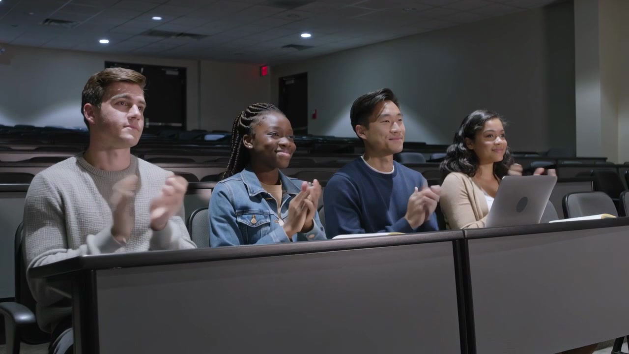 Clapping group of four students responding to speaker ending at university hall, laptop visible