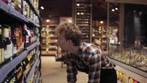 man in apron, store employee arranging bottles of beer, adding to the shelf in the supermarket. working in the section of alcoholic drinks. side view