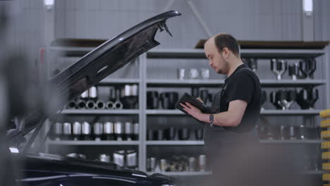 man mechanic at the hood of a car with a tablet diagnoses all systems and searches for malfunctions