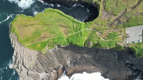 aerial drone shot flying over the coastal kilkee cliffs, in county clare ireland, with views of waves crushing over the rugged coastline