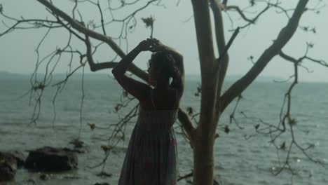 a woman silhouette stands in front of a tree by the water practicing yoga outdoors at the natural spot