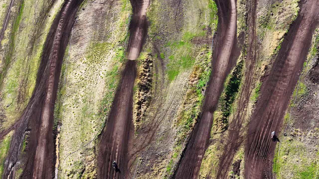 Drone captures single dirt bike riding along winding motocross track, natural daylight, top-down perspective