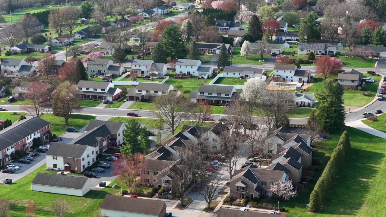 American suburban neighborhood with townhouse and single family houses in quiet residential area surrounded by green spring landscape and trees showing peaceful community living. Aerial drone view