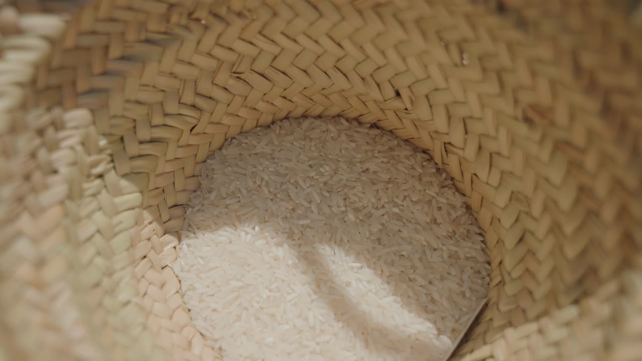 Primo piano di riso bianco crudo all'interno di un cesto di paglia rustico in una calda luce naturale.
