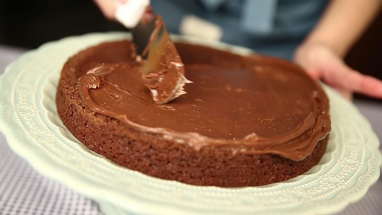 Espalhando um recheio de glacê de chocolate na primeira camada de um bolo caseiro