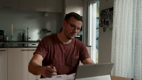 man in the kitchen in front of his laptop. massages his temples
