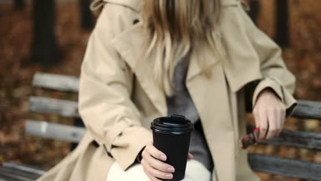 Unrecognizable-woman-drinking-coffee-sitting-on-park-bench