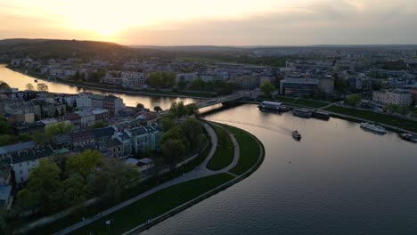 Weitwinkelaufnahme-Einer-Drohne-Bei-Sonnenuntergang-über-Der-Weichsel-In-Krakau,-Polen,-Mit-Leichtem-Dunst-Am-Himmel,-Der-Die-Sonne-Streut,-Während-Autos-über-Eine-Brücke-Fahren