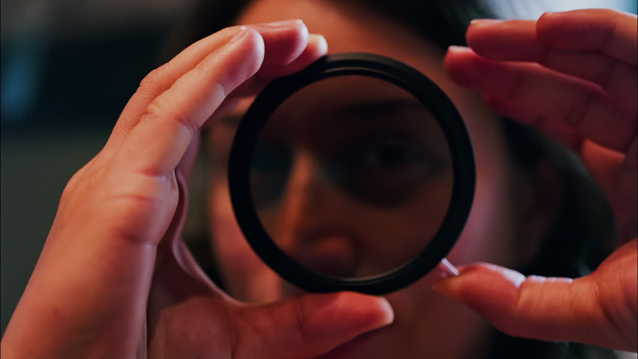 Close up of a woman rotating a camera lens filter near her face