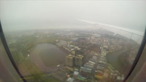 Landing-at-Taiwan-Taoyuan-International-Airport-on-a-cloudy,-rainy-winter-day-flying-over-buildings