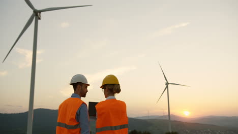 rear view of a man and woman in helmets discussing something at the huge windmills turbines