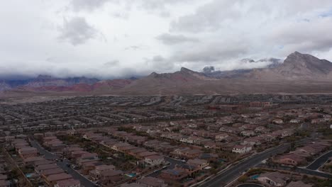 Aerial-wide-rising-shot-of-Red-Rock-Canyon-with-desert-suburban-community-in-the-foreground-in-Las-Vegas,-Nevada