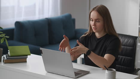 Una-Mujer-Joven-Se-Comunica-Por-Chat-En-Línea-En-Una-Reunión-A-Distancia-Con-Una-Computadora-Portátil-Hablando-Y-Gesticulando-Mirando-La-Pantalla-Remota-Trabajando-Desde-Casa