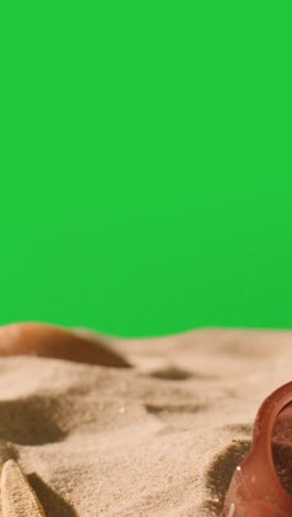 Vertical-Video-Summer-Holiday-Concept-Of-Sunglasses-On-Sand-Against-Green-Screen