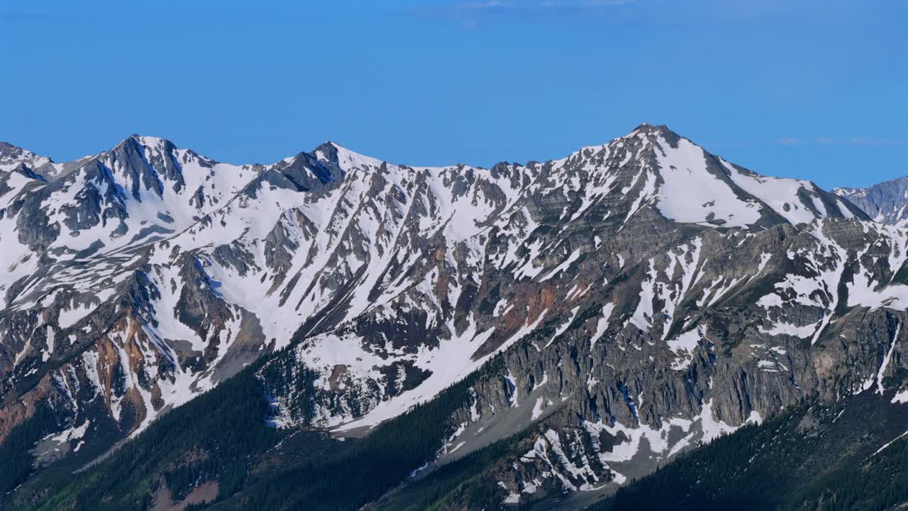Springtime summer melting snow cover Conundrum Castle Peak Rocky Elk Mountains range Ashcroft AJAX Aspen Mountain aerial drone Castle Creek Maroon Bells Wilderness sunny blue sky pan left motion